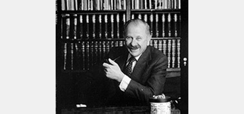 Mann im Anzug vor Bücherregal sitzend mit Pfeife, schwarz-weiß