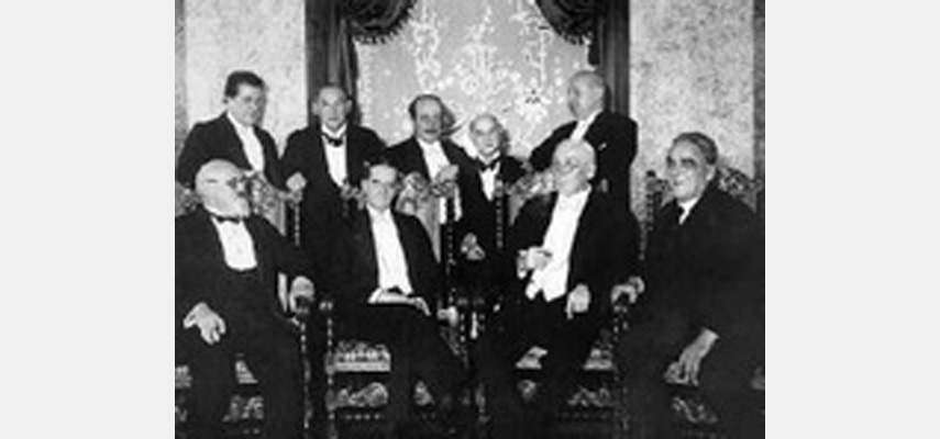 Neun Männer in Smokings vor eleganter Tapete für Foto posierend, schwarz-weiß