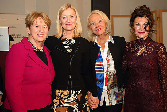 Vier Frauen in eleganter Kleidung posieren nebeneinander vor Rednerpult