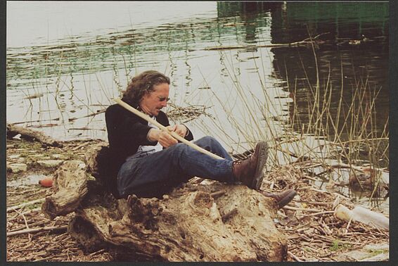 Foto von Mann, der neben Fluss auf einem Baumstamm liegt