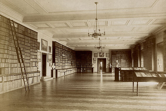 Sepia-Foto eines großen Saals mit Bücherregalen an den Wänden und Tischvitrinen