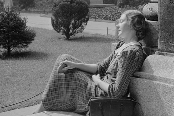 Junge Frau in kariertem Kleid sitzt in einem Hof und sonnt sich