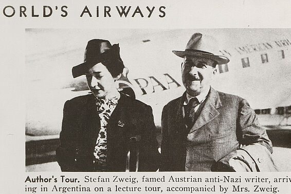 Schwarz-weißes Foto von Man und Frau in Hüten und Mänteln vor einem Flugzeug