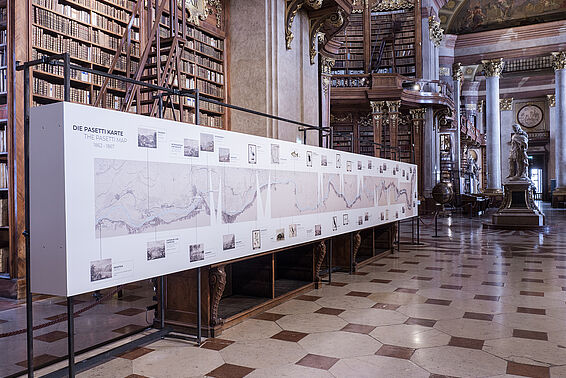 Stellage mit aufgedruckter Fluss-Karte in Marmorsaal vor Bücherregalen