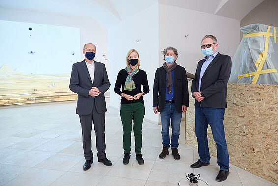 Eine Frau und drei Männer mit Mund-Nasen-Schutz stehen in einem Raum, der gerade renoviert wird