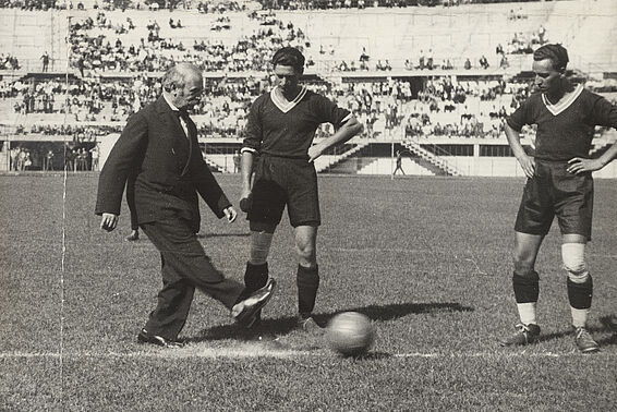 2 Fußballer und ein Mann im Anzug kicken auf dem Spielfeld, alte Schwarzweiß-Aufnahme