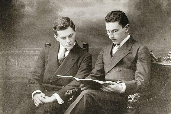 Zwei Männer sitzen nebeneinander und sehen sich Zeitschrift an, schwarz-weiß, Ludwig und Paul Wittgenstein Noten studierend, Foto: Carl Pietzner, 1909 – © Österreichische Nationalbibliothek