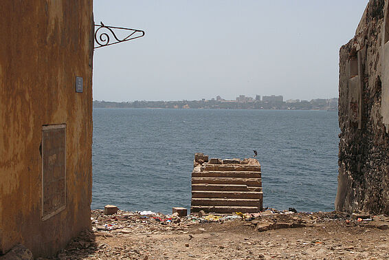 Blick von baufälligen Häusern über das Meer hin zu einer Stadt auf der anderen Küste