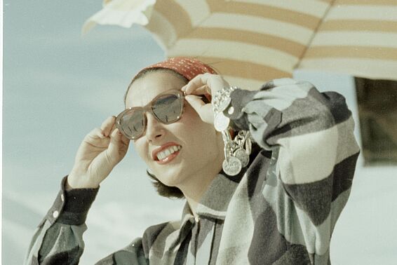 Frau mit kariertem Oberteil und Sonnenbrille unter Sonnenschirm
