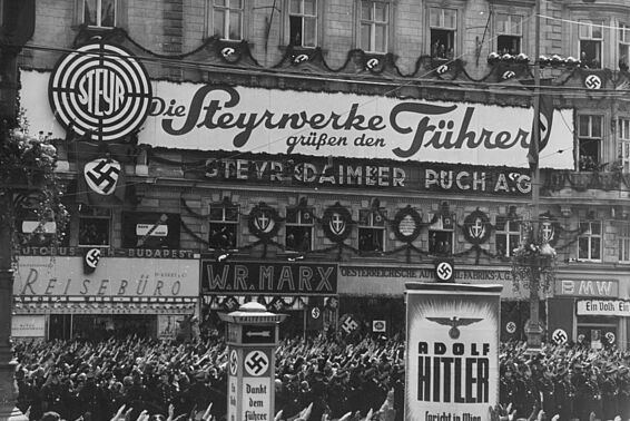 Menschenmenge macht Hitlergruß auf einer Einkaufsstraße, überall Nazi-Plakate