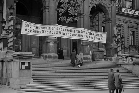 Treppenaufgang zu Universitätsgebäude mit Transparent, auf dem steht: "Sie müssen sich gegenseitig wieder achten lernen, der Arbeiter der Stirn und der Arbeiter der Faust."