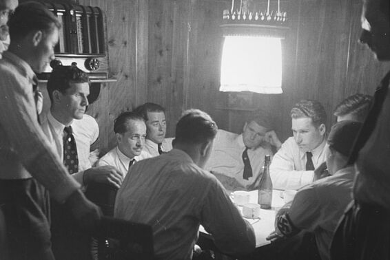 Gruppe von Männern sitzt an Tisch und hört Radio