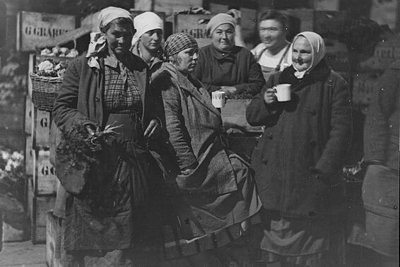 5 Frauen und ein Mann stehen auf einem Markt und trinken etwas