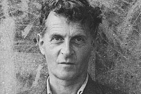 Schwarzweiß-Portrait von Ludwig Wittgenstein vor einer bemalten Mauer