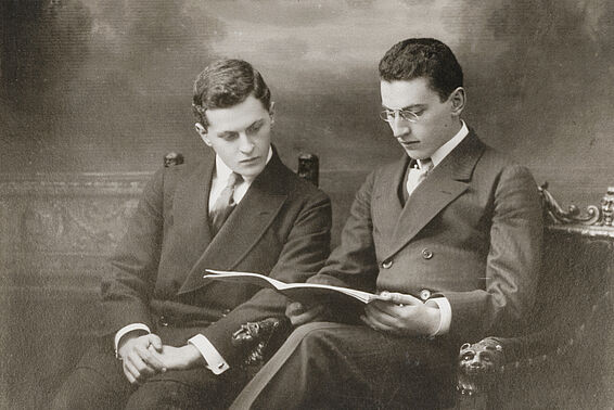 Zwei in Anzügen gekleidete Männer lesen in einem Heft, Schwarzweiß-Fotografie