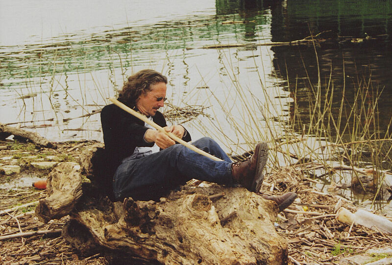 Mann sitzt in einem ausgehölten Baum neben einem Gewässer