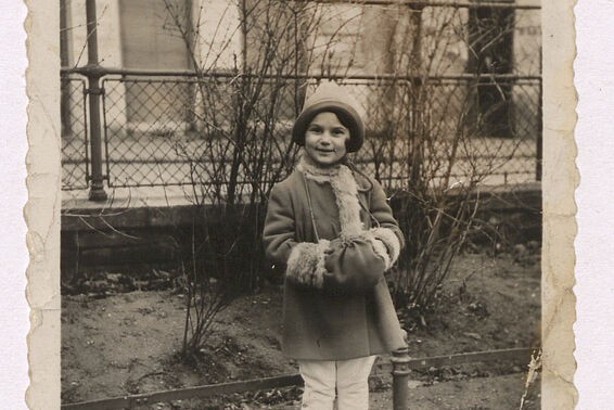 Old black and white photo of a small girl in winter clothes standing in a parc