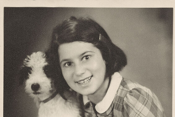Mädchen in kariertem Kleid posiert mit kleinem Hund für ein Porträtfoto, schwarz-weiß.