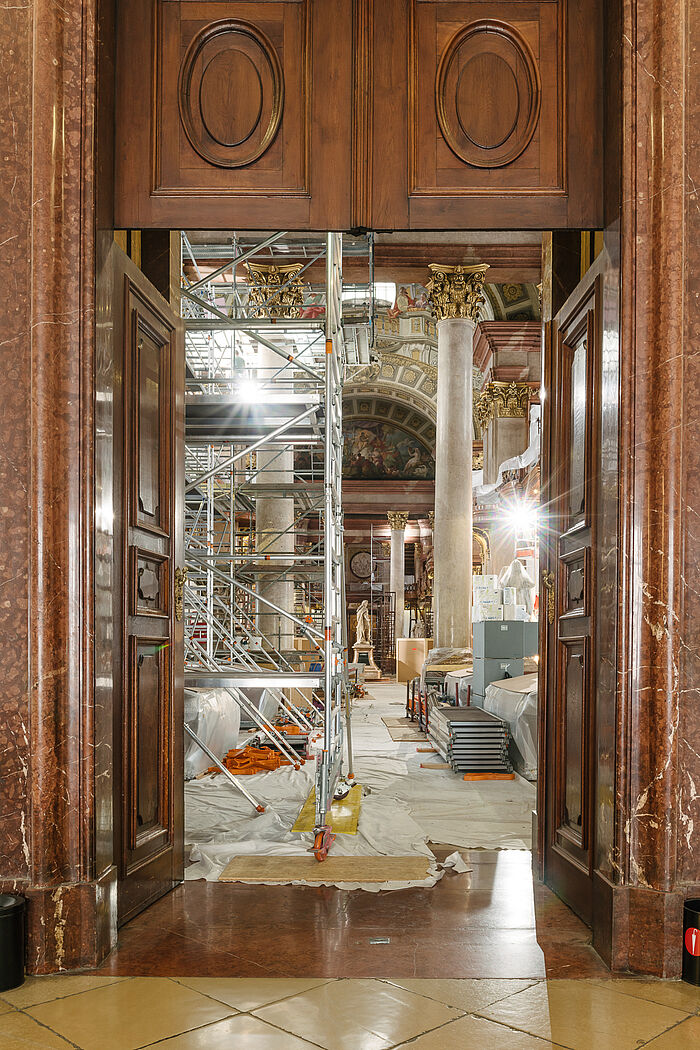 Blick durch Tür in Saal mit Statue in der Mitte, Baugerüsten und Planen am Boden.