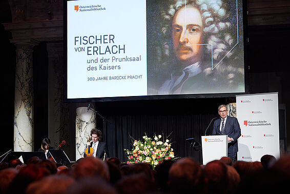 Mann mit Brille an Rednerpult vor Leinwand