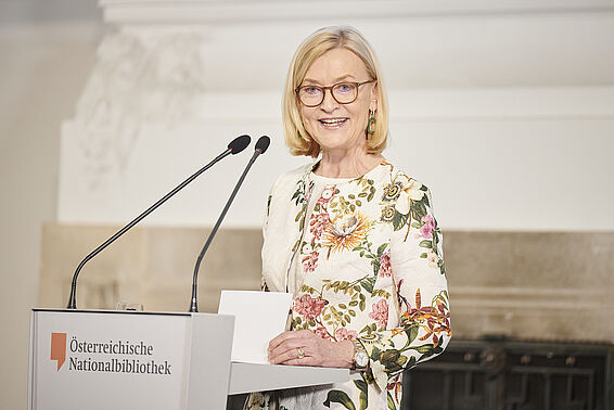 Blonde Frau mit geblümten Blazer an Rednerpult