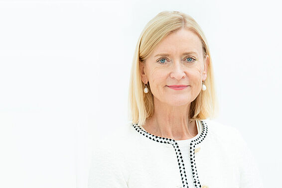 Porträtfoto von einer blonden Frau in weißer Jacke, die an einem Geländer lehnt