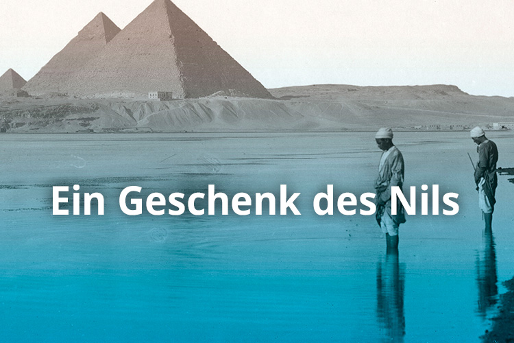 Zwei Personen stehen im Wasser, dahinter Pyramiden. Text: Ein Geschenk des Nils