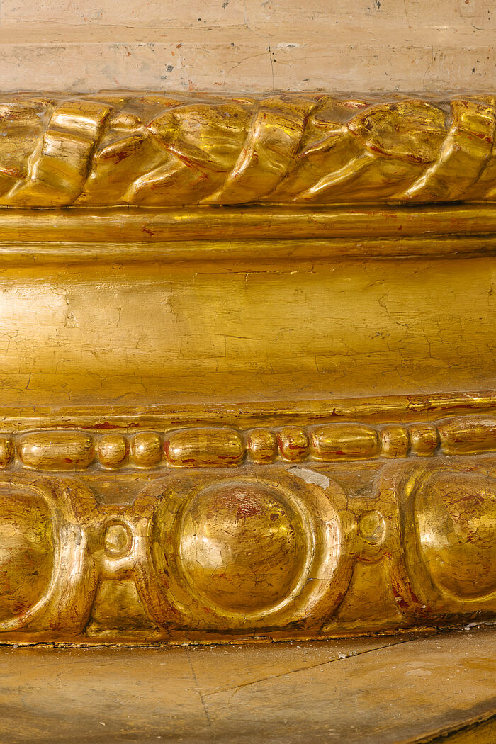 Nahaufnahme von abgesplitterter Goldverzierung an Säule.