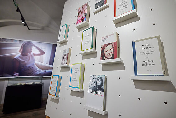 Museumsraum mit einen Foto an der Wand, im Vordergrund ein Regal mit Büchern.