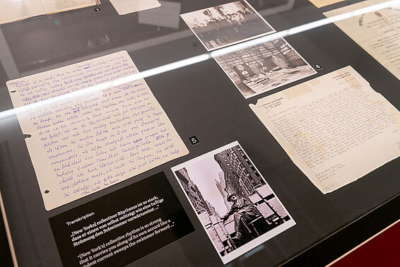 Tischvitrine mit handgeschriebenen Zetteln und schwarz-weißen Fotos.