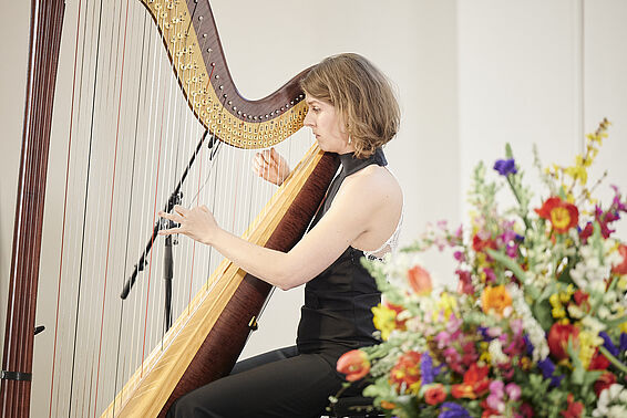 Harfenistin in Aktion neben bunten Blumenstrauss