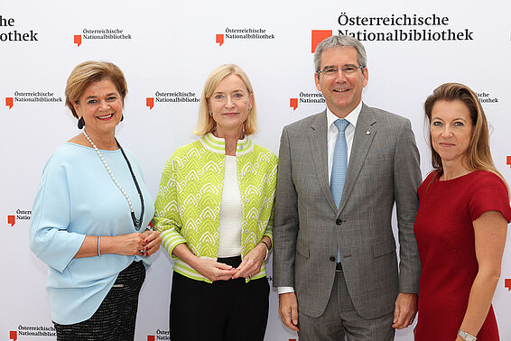 Drei elegant gekleidete Frauen und ein Mann im grauen Anzug