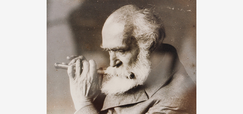 Foto von Mann mit Glatze und weißem Bart, der Querflöte spielt, schwarz-weiß.