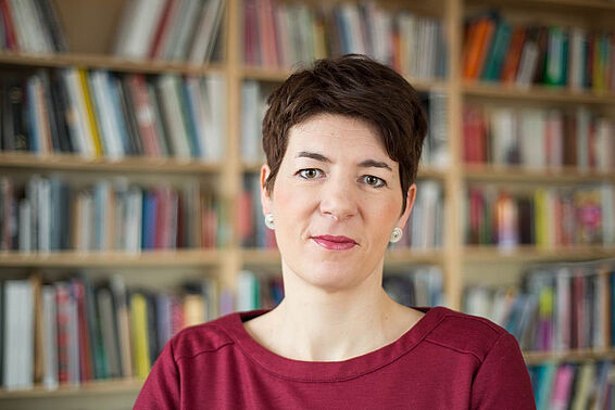 Porträtfoto von Frau mit kurzen, dunklen Haaren vor einem Bücherregal