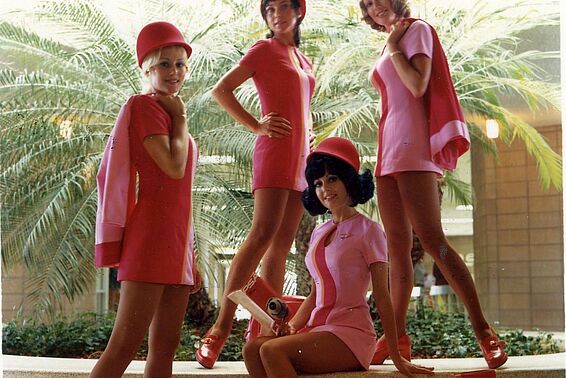 Foto von vier Frauen in pinken Uniformen, die vor einer großen Pflanze posieren.