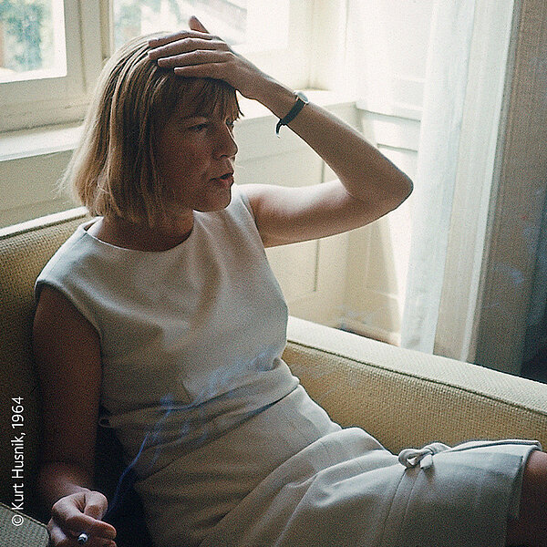 Foto von sitzender Frau in weißem Kleid, die sich an den Kopf greift