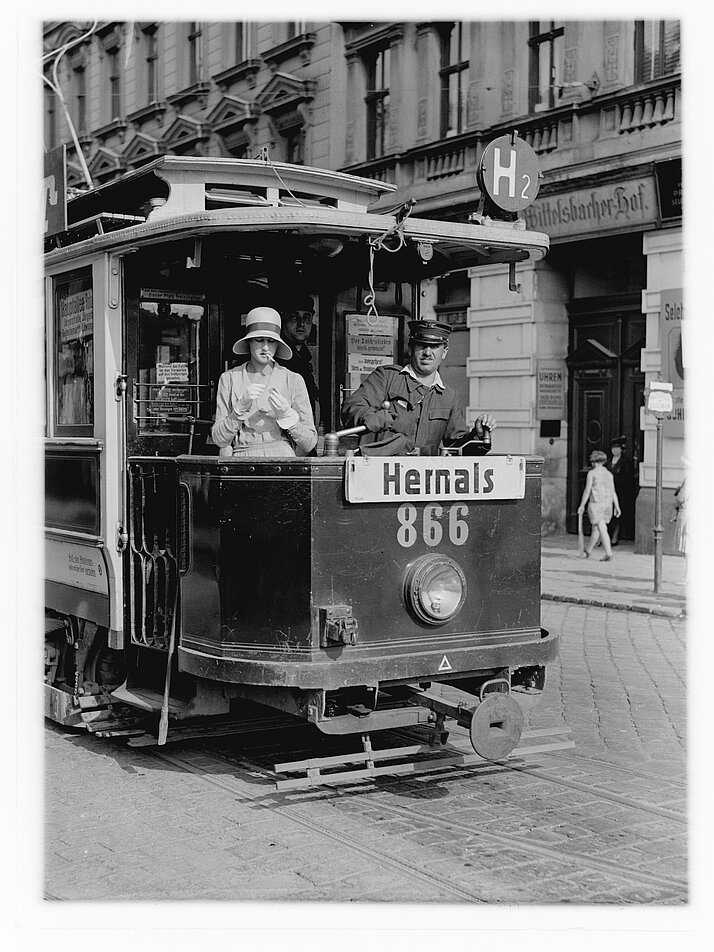 Frau steht im Aussenbereich der Straßenbahn und zündet sich neben der Schaffner eine Zigarette an