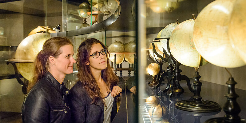 Zwei Personen betrachten Globen in einer Vitrine
