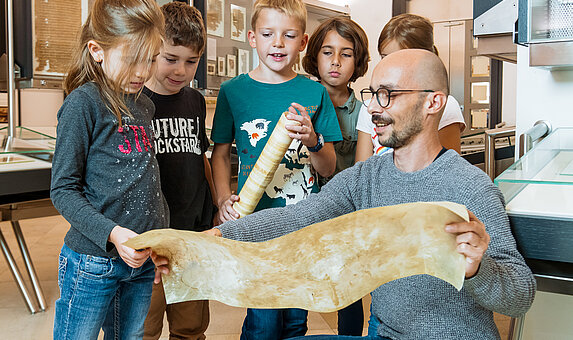 Eine Kindergruppe betrachtet im Rahmen einer Führung ein Stück Pergament.