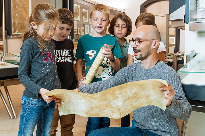 Eine Kindergruppe betrachtet im Rahmen einer Führung ein Stück Pergament.