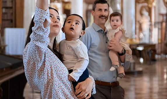 Zwei Personen mit Babys am Arm in einem prächtigen Saal