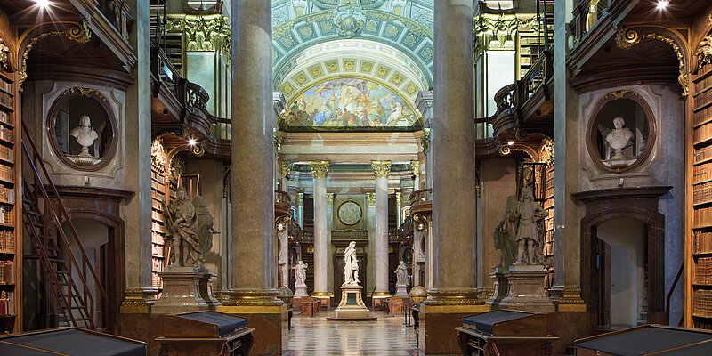 Foto von Marmorsaal mit Statue und Bücherregalen sowie Deckenfresko.