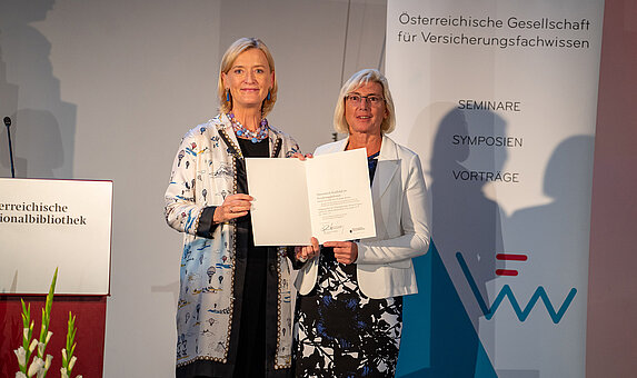 Zwei Personen halten eine Urkunde auf einer Bühne.