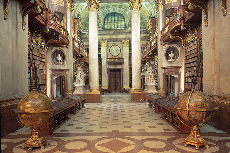 Alter, prunkvoller Bibliotheksraum mit zwei prächtigen Globen im Vordergrund.