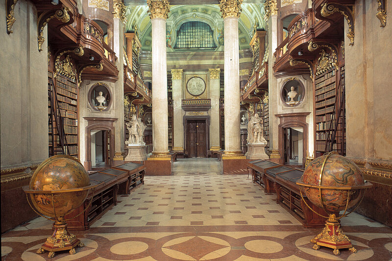 Alter, prunkvoller Bibliotheksraum mit zwei prächtigen Globen im Vordergrund.