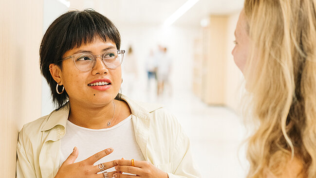 2 Personen stehen in einem hellen Foyer und unterhalten sich