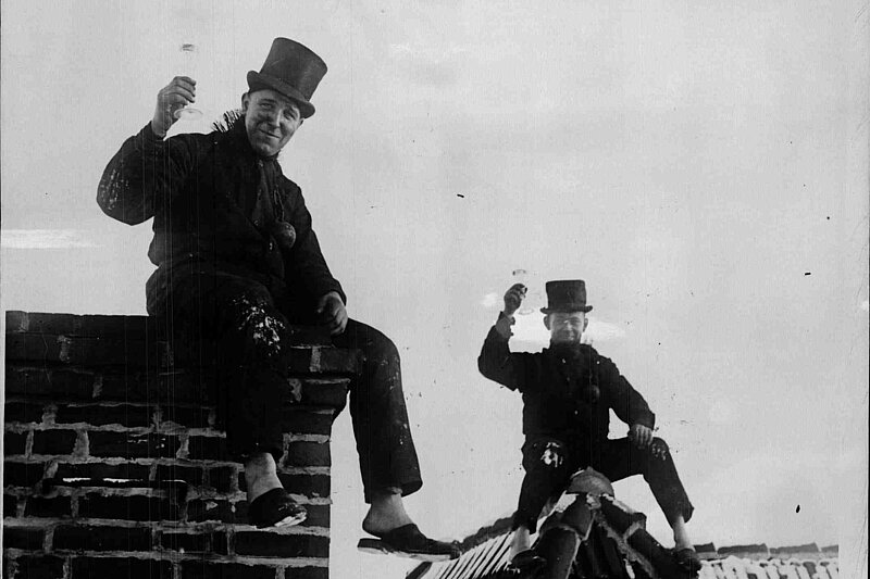 Teaserbild.jpg Schwarz-weißes Foto von zwei Rauchfangkehrern, die auf Dächern sitzen und Sektgläser hochhalten.