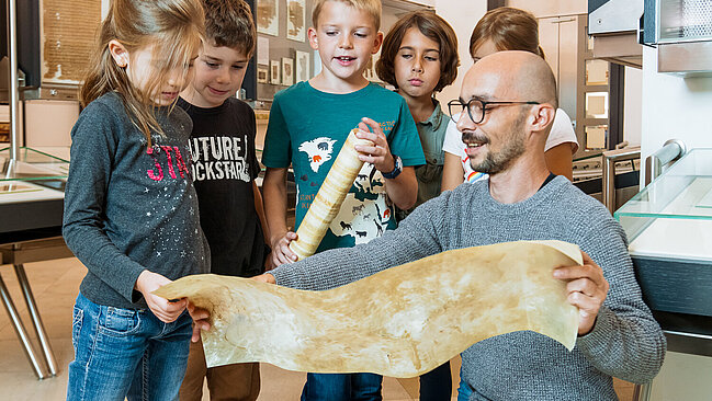Children are looking at a piece of parchment during a guided tour.