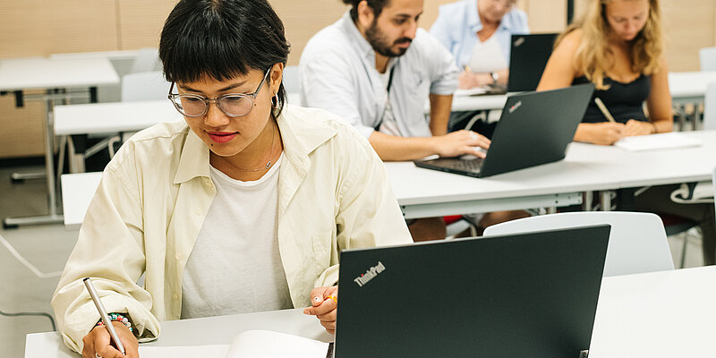 Mehrere Personen sitzen vor Laptops und machen sich Notizen 