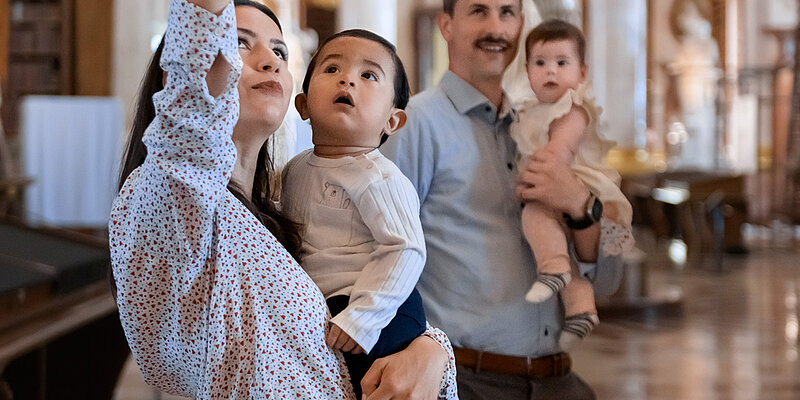 Zwei Personen mit Babys am Arm in einem prächtigen Saal